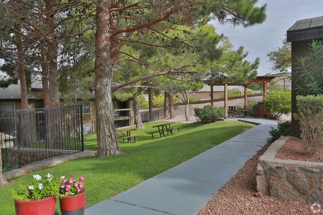 Walkway through a grassy courtyard with picnic tables and trees.