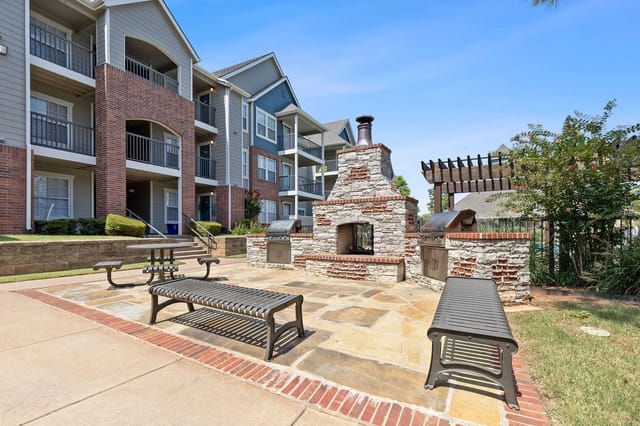 Outdoor community grilling area with stone fireplace and benches.