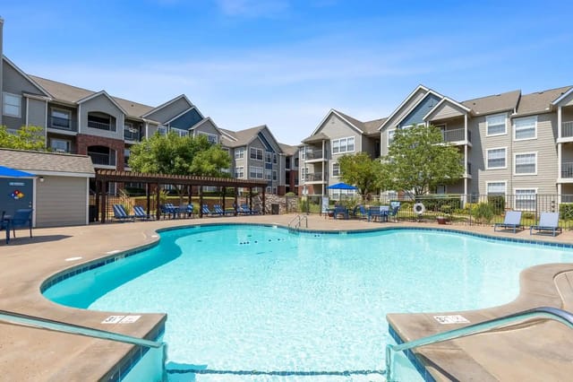 Outdoor pool area with lounge chairs and shaded seating, surrounded by apartment buildings.