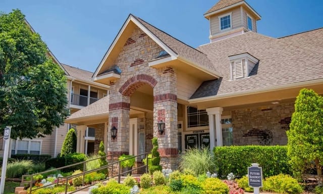 Exterior view of an apartment community entrance with stone facade and manicured landscaping.