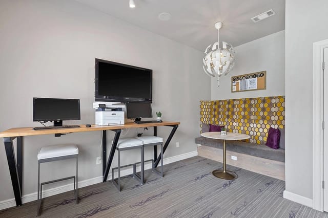 Community lounge with workstation desk, screens, printer, and cozy seating nook.