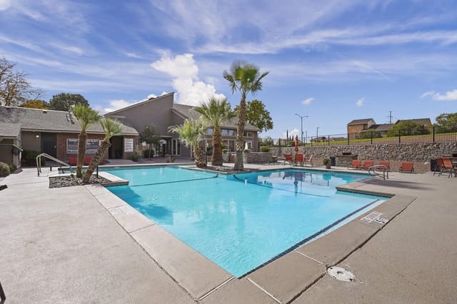 Swimming pool and lounge chairs with palm trees and apartment buildings in the background.