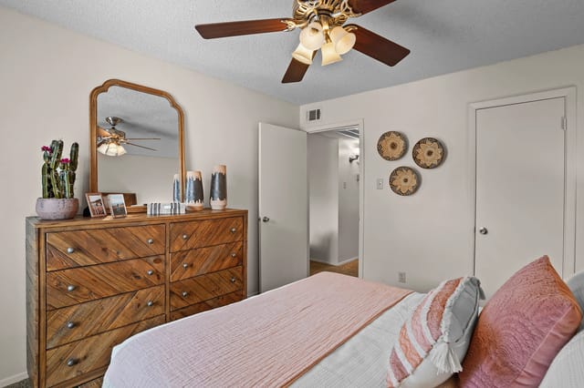 A bedroom with a dresser, mirror, bed, and ceiling fan.