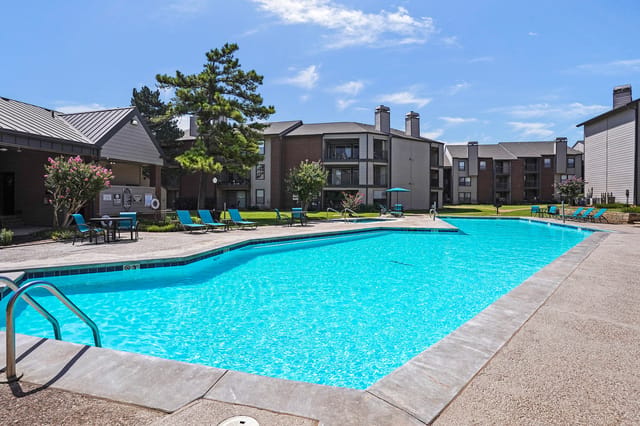 Resort-style outdoor swimming pool with lounge chairs and surrounding apartment buildings.