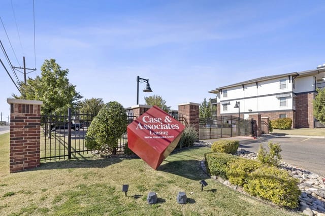 Gated apartment community entrance with brick columns and a red leasing sign.