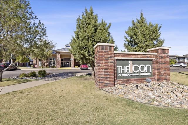 Exterior view of a brick sign for The Icon apartment community with landscaping.