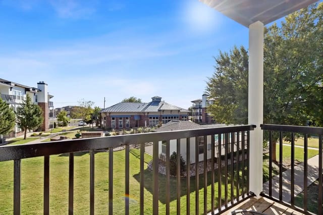 Balcony view of a sunny apartment community courtyard with clubhouse, walkways, and trees.