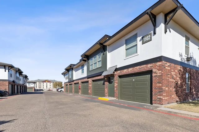 Row of two-story townhomes with brick bases and attached garages along a wide street.