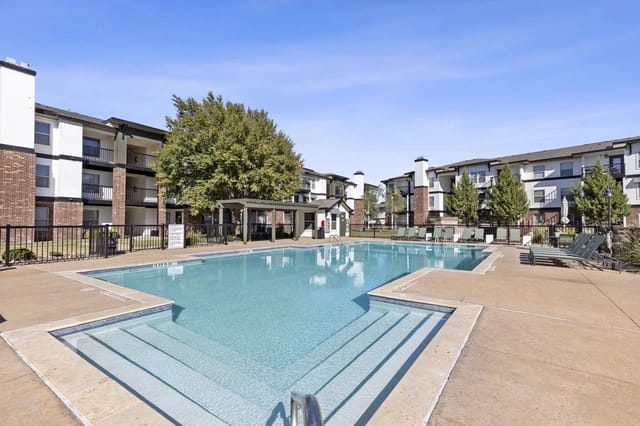 Outdoor communal pool with steps, lounge chairs, and surrounding apartment buildings.