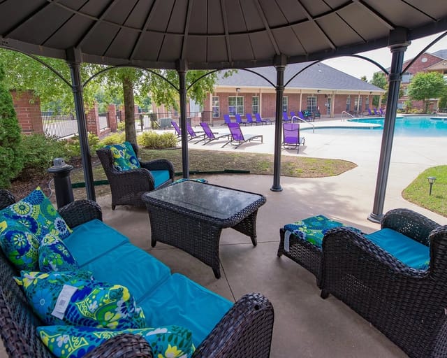 Covered outdoor seating under a gazebo with a swimming pool and purple lounge chairs in the background.
