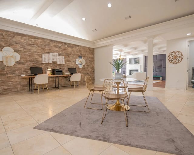 Modern apartment lobby with a stone accent wall, desks, and gold chairs.