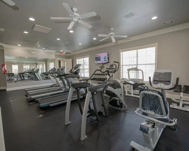 Interior of a residential community gym with treadmills, ellipticals, bikes, and mirrors.