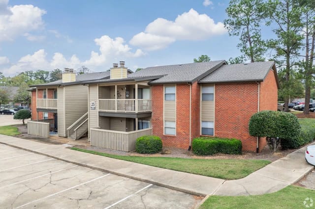 Exterior view of a brick apartment building with balconies and a parking lot.