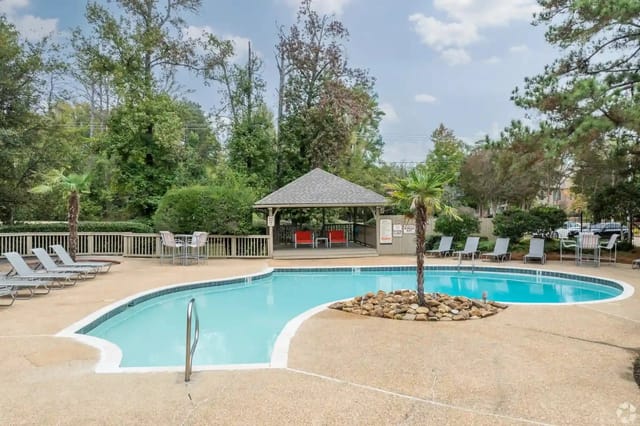 Outdoor community pool area with lounge chairs, a shaded gazebo, and surrounding trees.