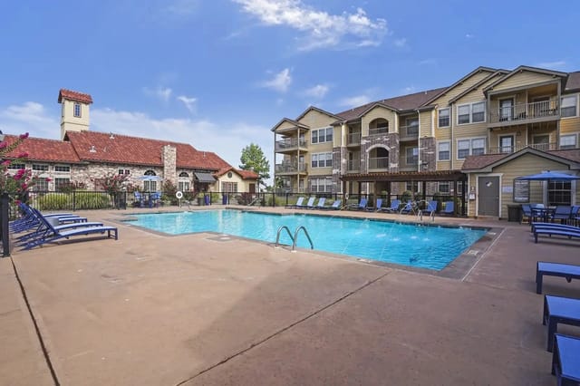 Outdoor pool deck at a multifamily community with lounge chairs and surrounding buildings.