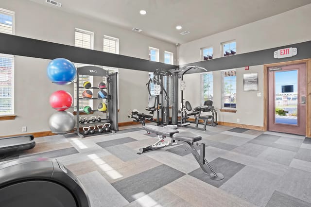 Bright communal fitness center with weight machines, kettlebells, medicine balls, and cardio equipment.