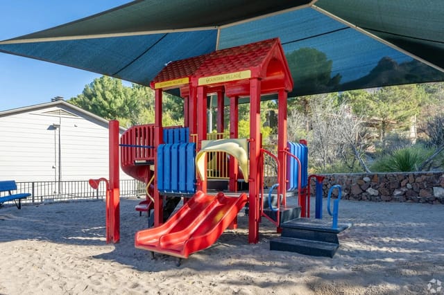 Playground with red and blue structures under a blue sunshade.