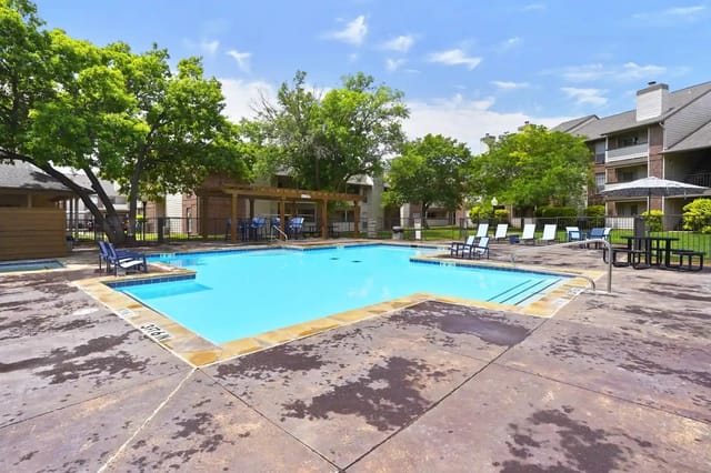 Outdoor communal pool with blue water, lounge chairs, and a shaded seating pavilion.