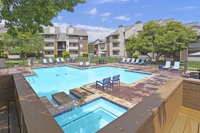 Outdoor community pool with blue water, lounge chairs, and surrounding apartment buildings.