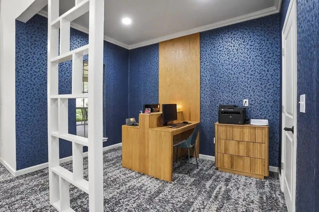 Interior apartment office with wood desk, computer, and printer against blue patterned wallpaper.