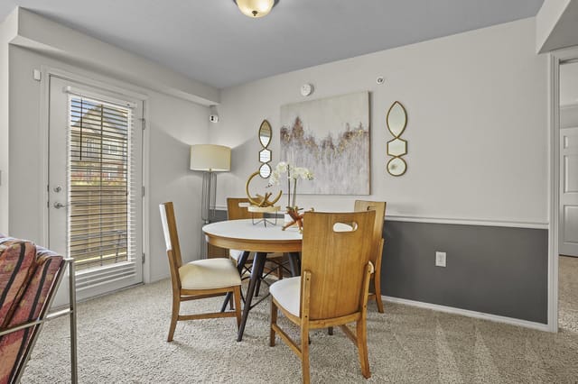 Interior dining area in an apartment with a round table, wooden chairs, and wall art.
