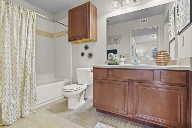 Bathroom with wood vanity, mirror, toilet, and a shower/tub with a patterned curtain.