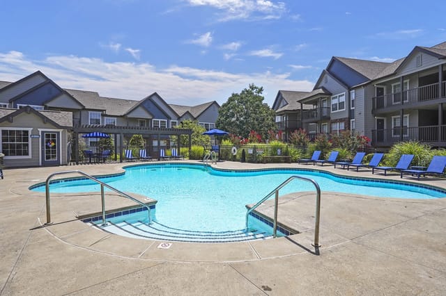 Outdoor apartment community pool with blue lounge chairs and surrounding buildings.