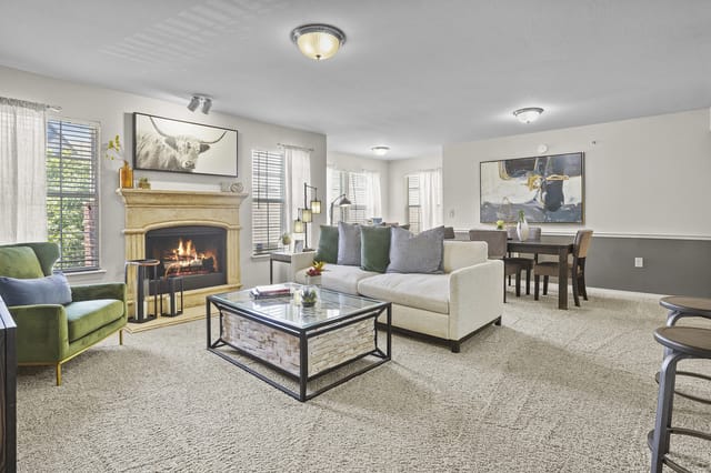 Bright living room with beige sofa, green armchair, stone fireplace, and a dining area.