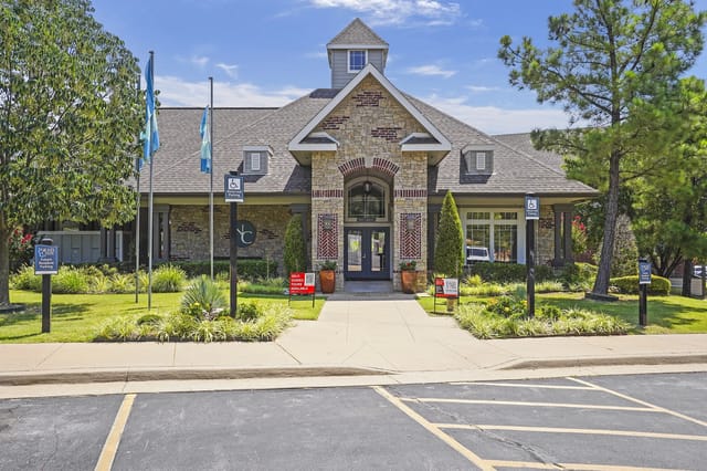 Exterior of a stone-faced apartment community entrance with flags and landscaping.