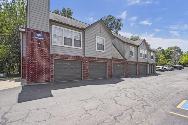 Exterior row of townhouse-style buildings with attached garages and a brick base.