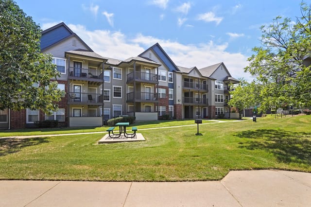 Apartment building exterior with balconies, green lawn, picnic table, and grill.