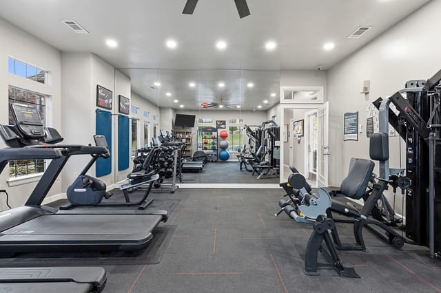 Interior view of a well-equipped apartment fitness center with treadmills, weight machines, dumbbells, and mirrors.