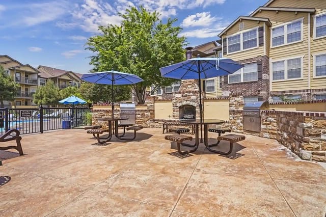 Outdoor seating area with picnic tables, umbrellas, grills, and a fireplace.