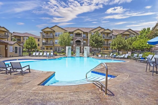 Resort-style swimming pool with lounge chairs and surrounding apartment buildings.
