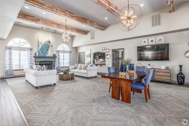 Bright community lounge with sofas, a dining table, large arched windows, and a wall-mounted TV.