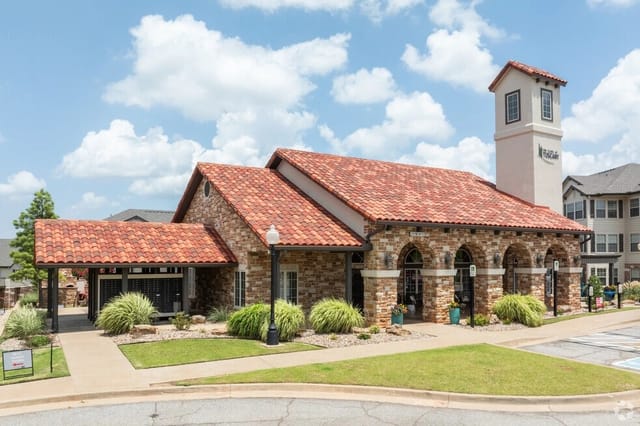 Exterior view of a stone-clad clubhouse with arches and a red-tiled roof at an apartment community.
