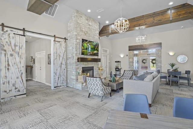 Open-concept community lounge with a stone fireplace, high wood-beam ceiling, and comfortable seating.