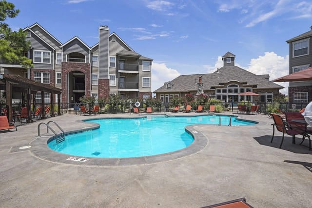 Outdoor pool area at an apartment community with lounge chairs and surrounding buildings.