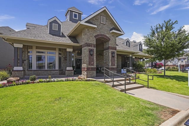 Exterior apartment building entrance with stone columns, ramp and landscaped lawn.