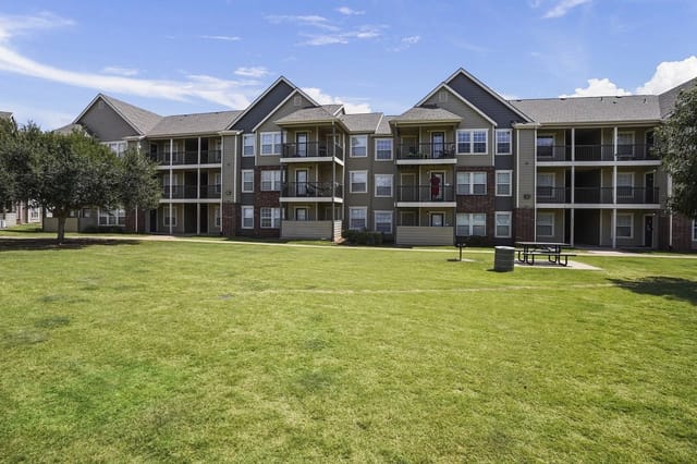 Exterior view of a multi-building apartment complex with balconies and a large grassy lawn.