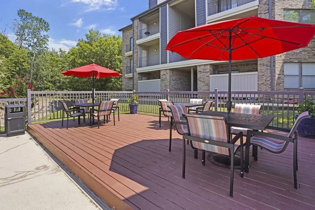 Outdoor communal deck with tables, chairs, and red umbrellas at an apartment complex.