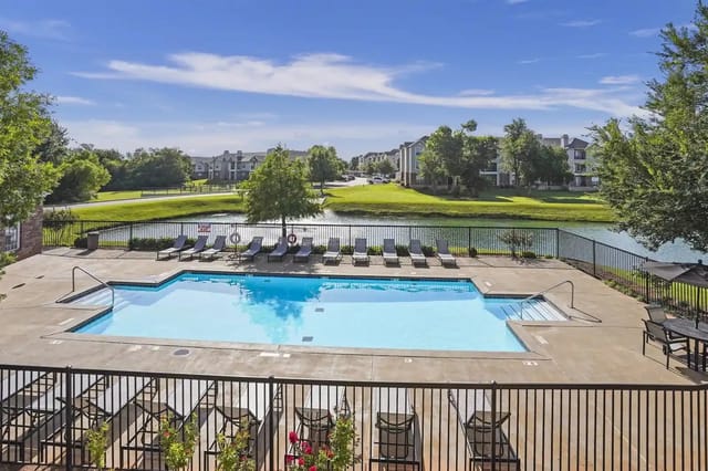 Outdoor communal swimming pool with lounge chairs and a pond beyond, with apartment buildings in the background.