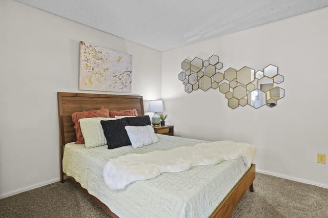 Bedroom with a queen-size bed, wooden headboard, decorative pillows, and wall art.