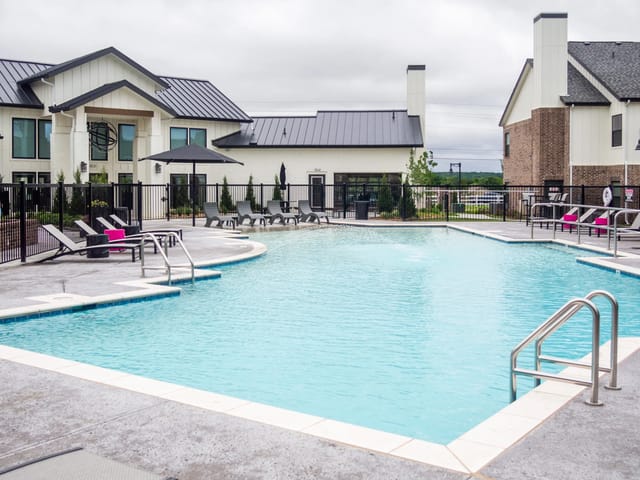Outdoor community pool at a multifamily property with lounge chairs and a black fence.