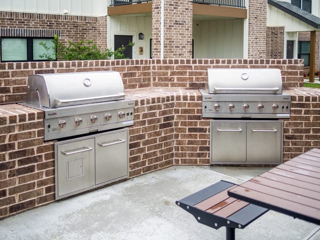 Two stainless steel outdoor grills set into brick counters in a communal patio.
