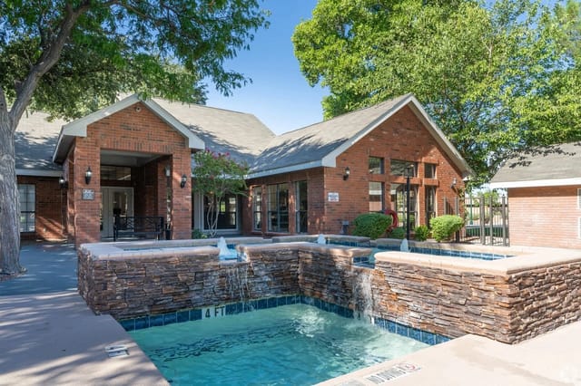 Outdoor community pool with brick buildings, stone water feature, and trees.