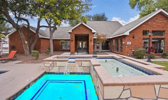 Outdoor brick apartment community center with a pool, hot tub, and surrounding lounge area.