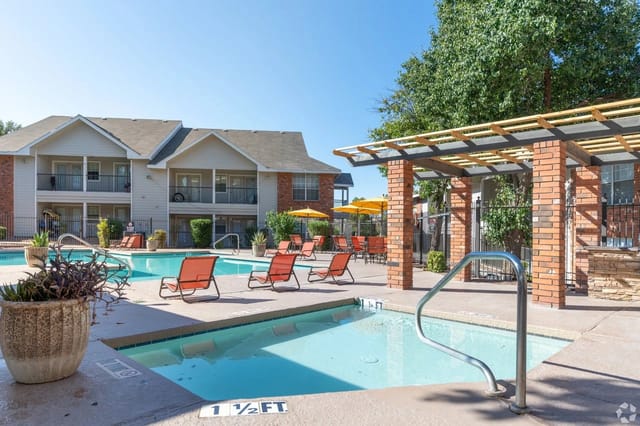 Outdoor apartment pool with orange lounge chairs and brick pergola.
