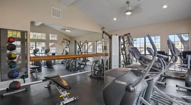 Indoor apartment gym with cardio machines, weights, and mirrors.