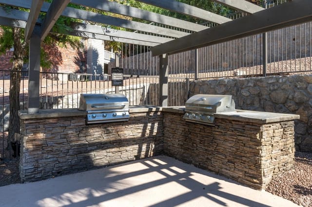 Outdoor grilling station with two built-in grills set on a stone counter under a pergola.